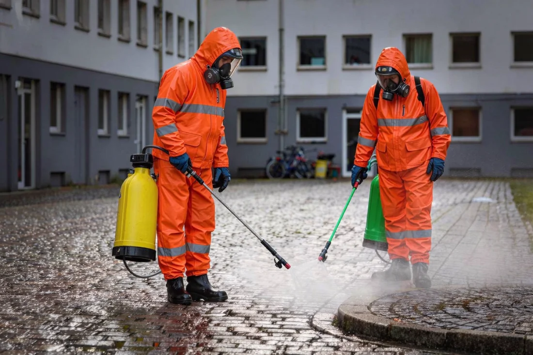 Pracovníci dezinfikují dvůr bytového domu po úniku splašků